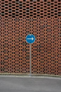 A blue right-turn sign stands in front of a wall made of interlocking red bricks, almost like a visual 3xx redirect guiding your path.