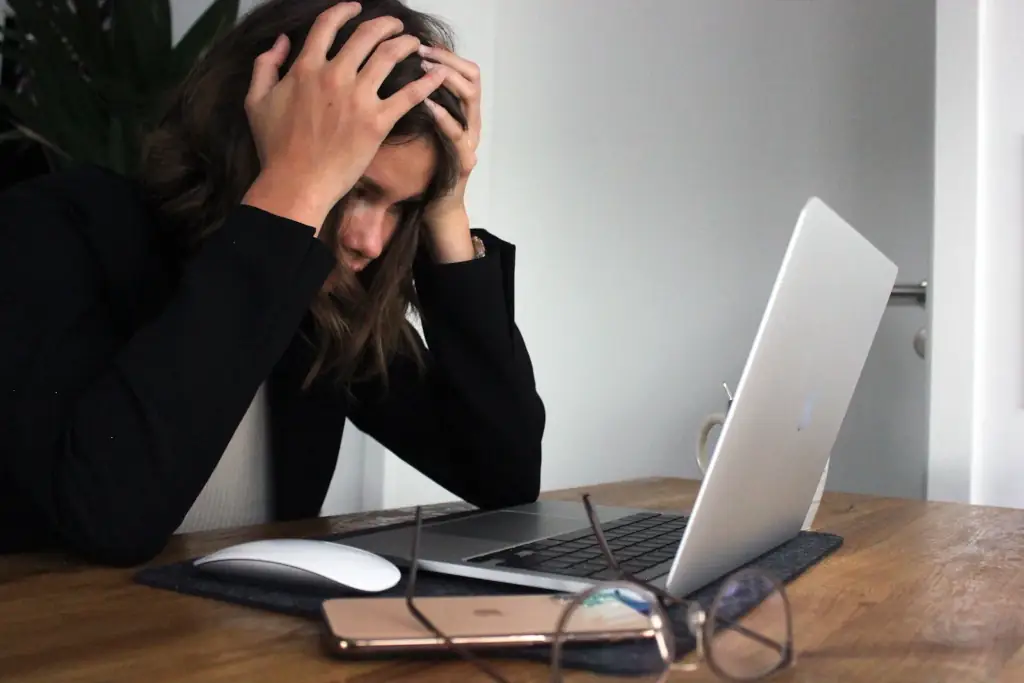 A woman is holding her head in front of her laptop while contemplating the need for a SEO consultant to audit her site.