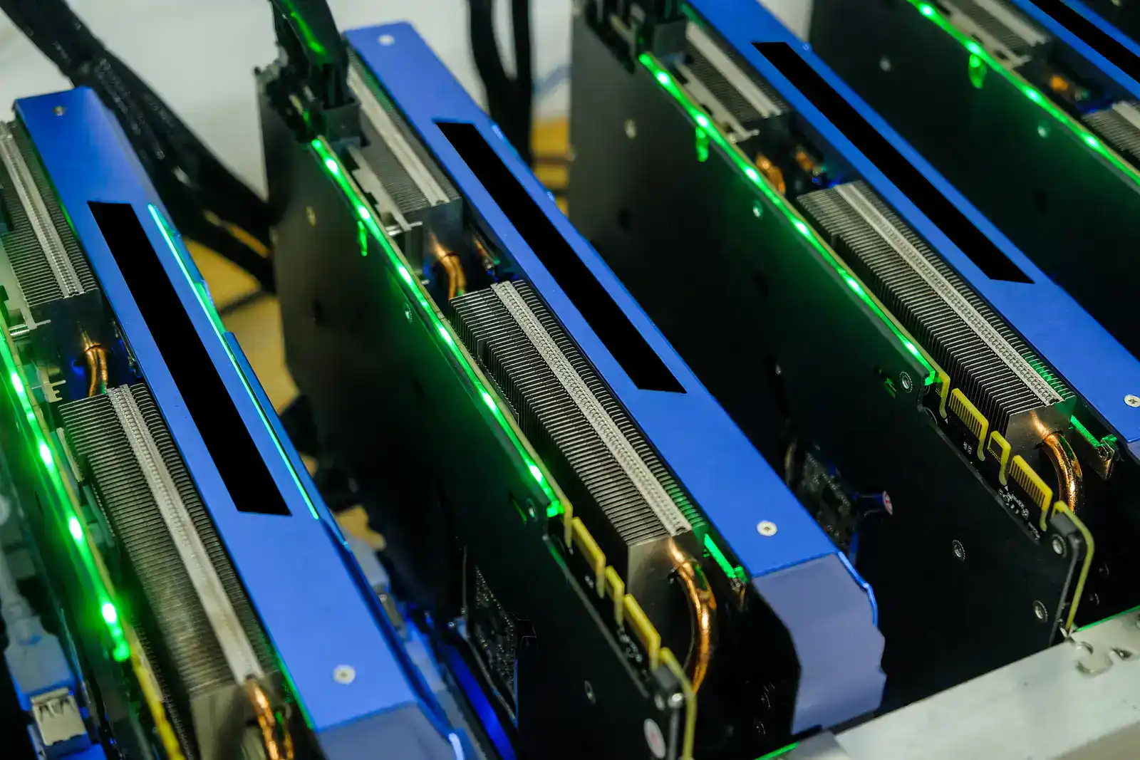 Close-up of multiple GPUs installed in a computer rig, with green indicator lights showing they are active.