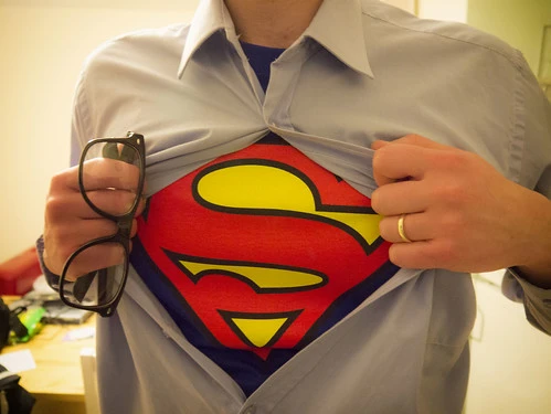 Person wearing a Superman t-shirt under a button-up shirt, pulling the shirt open to reveal the Superman logo.