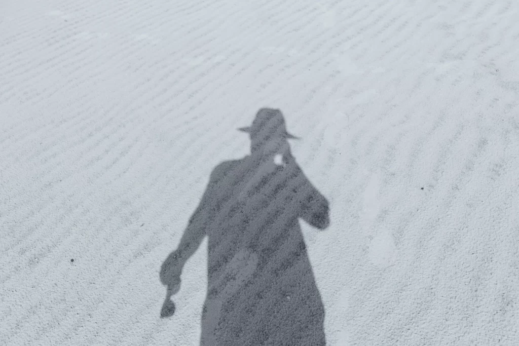 Shadow of a person wearing a hat on rippled sand, holding something—like theyre monitoring real user activity.